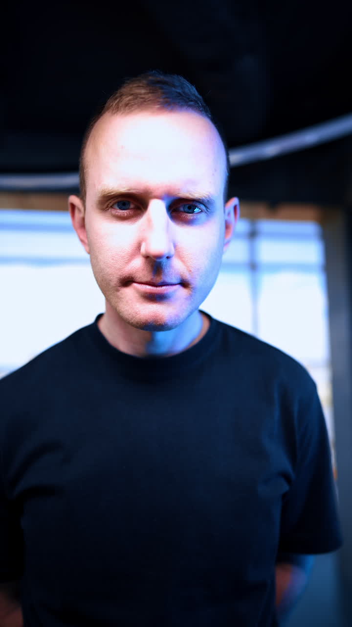 Confident Caucasian male in the room with light flashing looks straight at camera. Portrait of a man gazing at you. Close up. Vertical video.