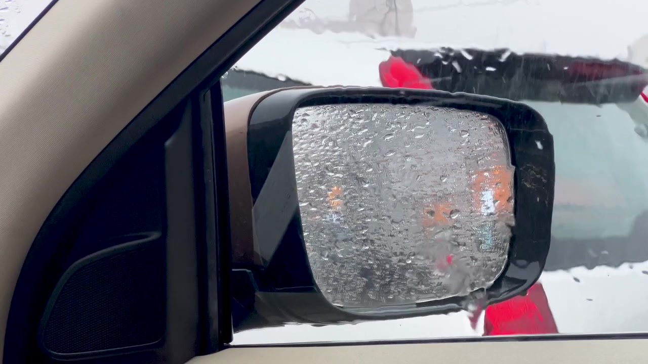 Close up of a vehicle side wing mirror coated in thick ice and frozen rain drops during a cold winter blizzard. Useful for weather reports and winter safety content.