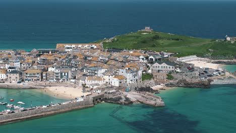 High dolly left tracking aerial along coast of St. Ives showing rooftops and boats under sunny blue sky day