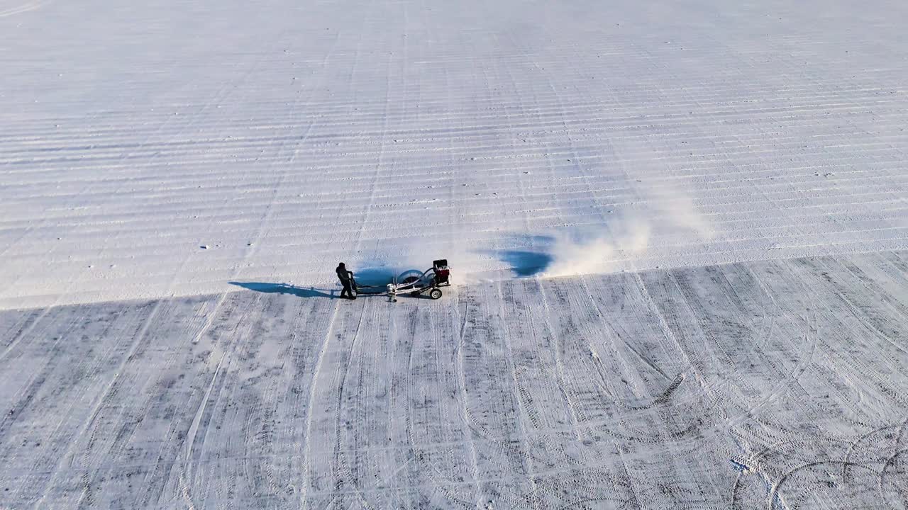 Aerial shot of an ice-cutting machine working on the frozen Songhua River in Harbin, during the Ice Festival. The machine carves through the thick ice, creating a trail of snow. China