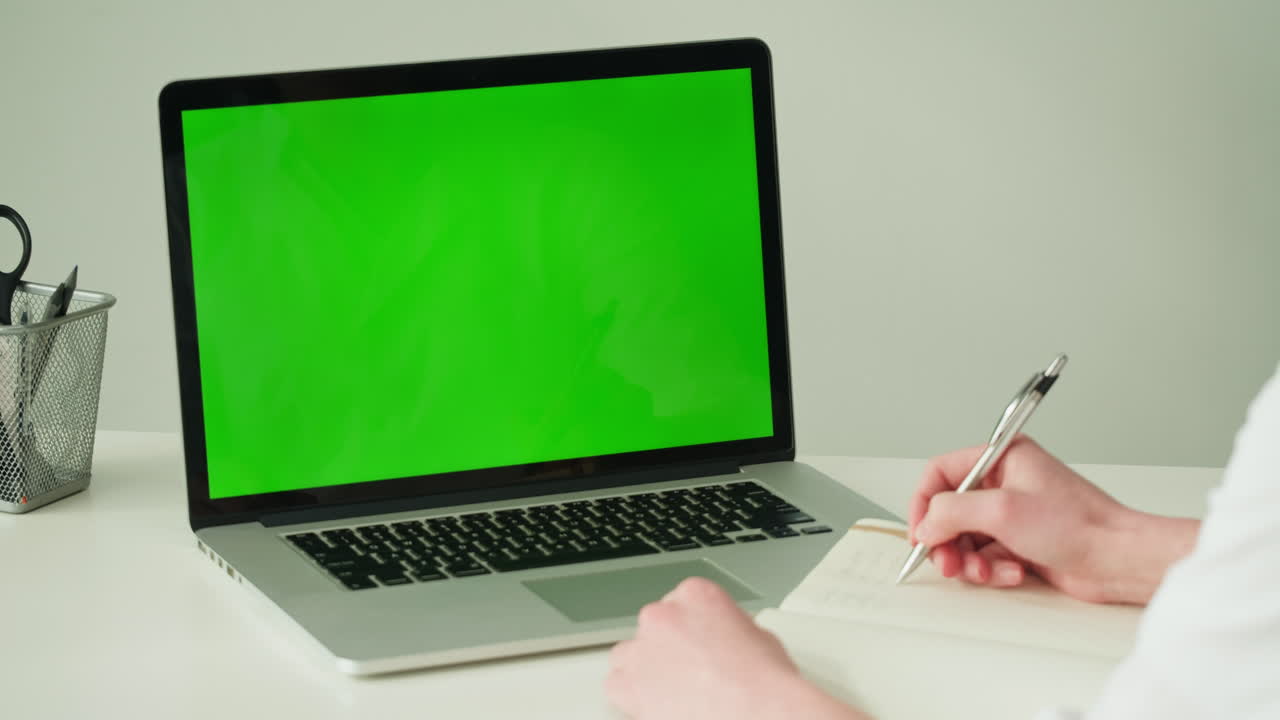 Person taking notes on a laptop with a green screen