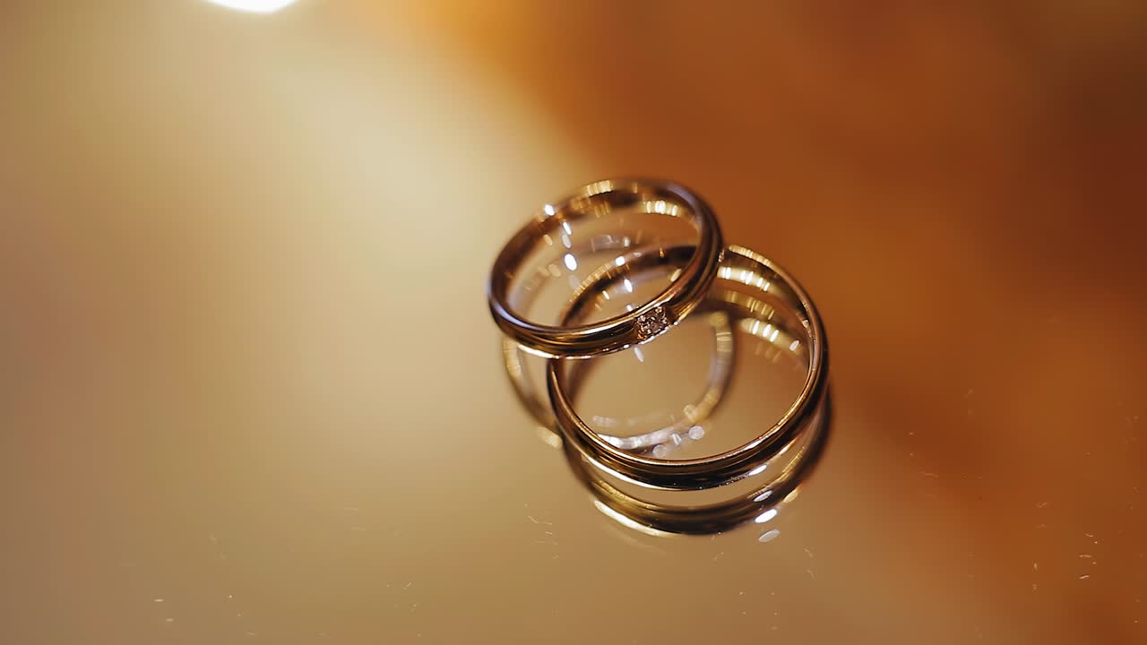 두 개의 금 반지는 거울 표면에 놓여 있고 아름다운 하이라이트로 빛납니다.