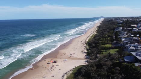 drone hoovering then ascending over a sandy beach, beachside town in the background