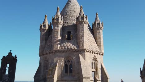 hyperlapse: aerial flight past adult woman walking alone on walkway crossing towards old historic granite evora cathedral conical spire lantern tower with medieval tile roof, aerial approach tilt up