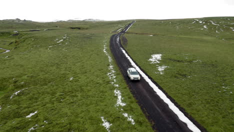 aerial front view: one car driving on a muddy mountain road partially covered with snow
