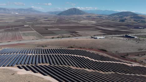 Drone-over-photovoltaic-solar-power-farm-row-panels-tilt-down-highway-street-sunny