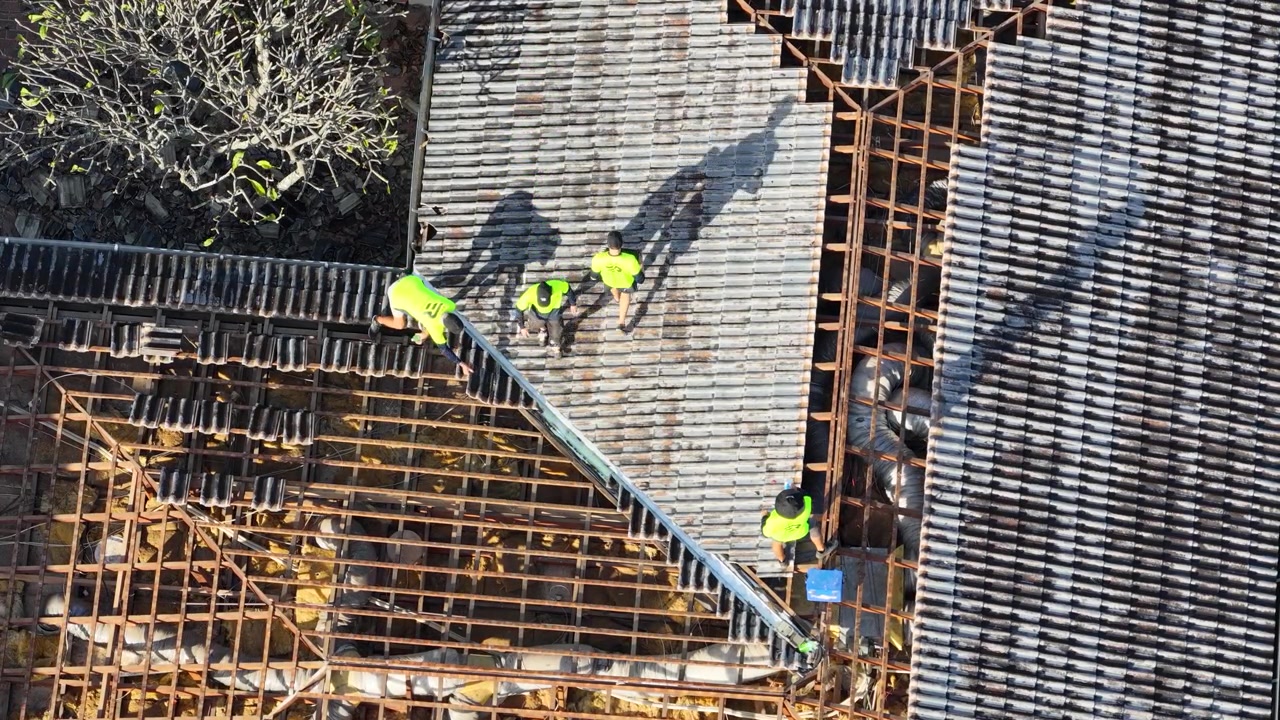 Top-down drone shot of contractors in high-visibility vests performing maintenance on a house roof.