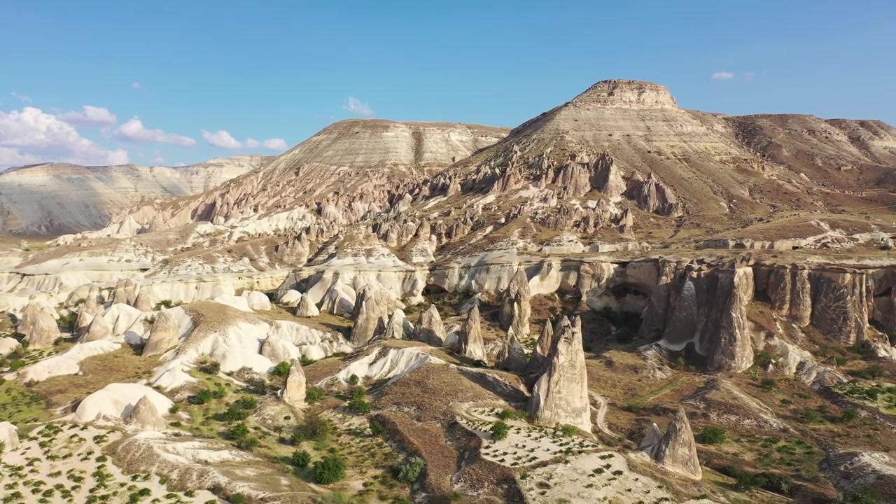 Panoramiczny widok z drona na białe formacje skalne, stożkowe kominy wróżek i płaskie góry tufowe w Dolinie Róż, Kapadocji, Nevsehir, Turcja, pod czystym błękitnym niebem
