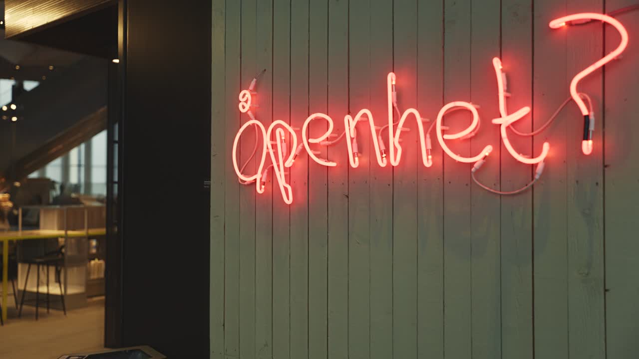 A neon sign reading "åpenhet?" translated to ''openness?'' mounted on a dark green wall, adding a modern and artistic touch to the library.