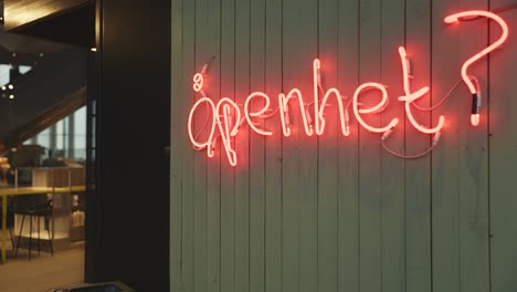 a neon sign reading "åpenhet?" translated to ''openness?'' mounted on a dark green wall, adding a modern and artistic touch to the library.