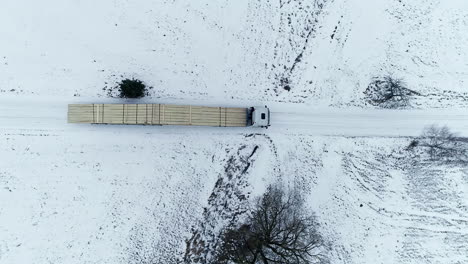 aerial top down shot of long truck transporting cleared wooden tree trunks on snowy winter day