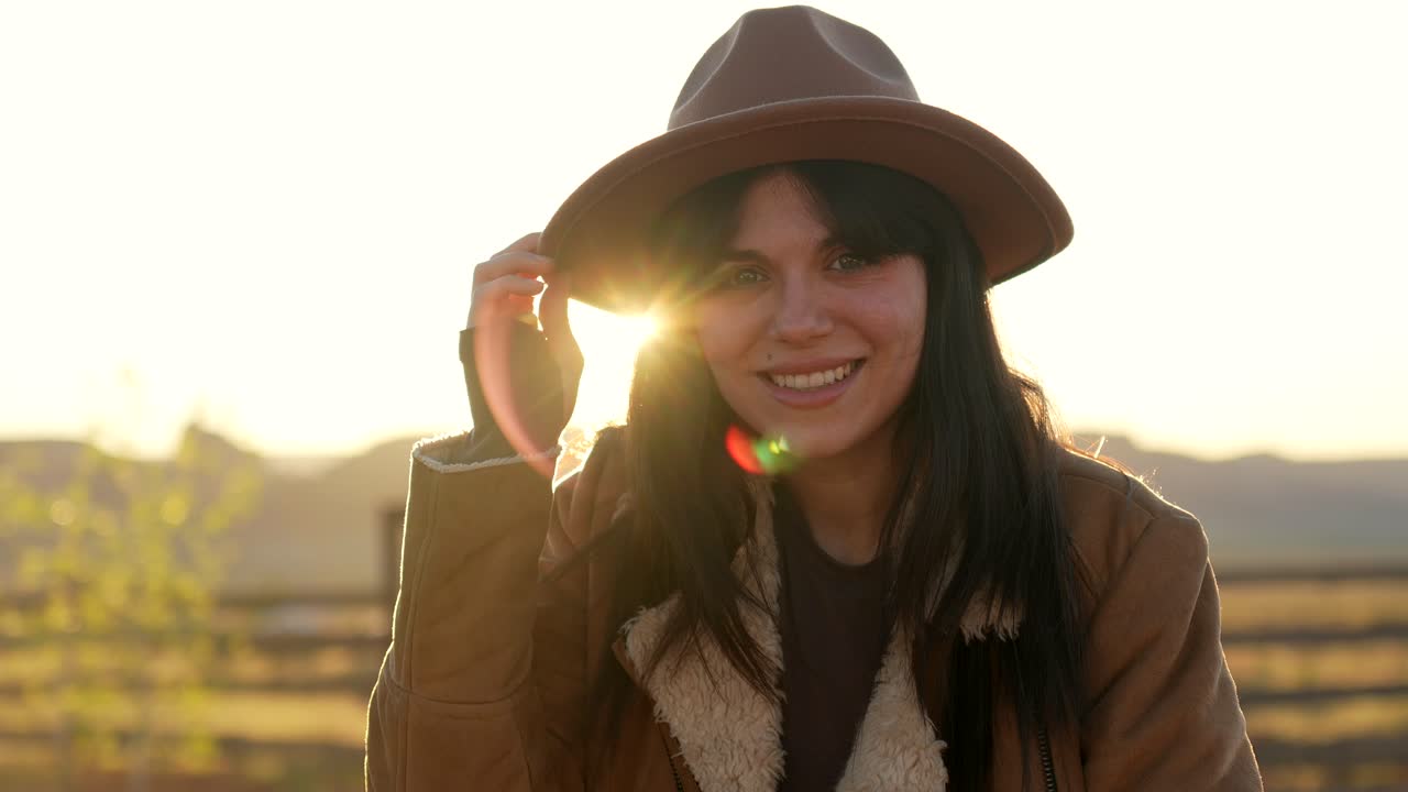 Giovane donna sorridente con cappello durante l'ora d'oro al tramonto