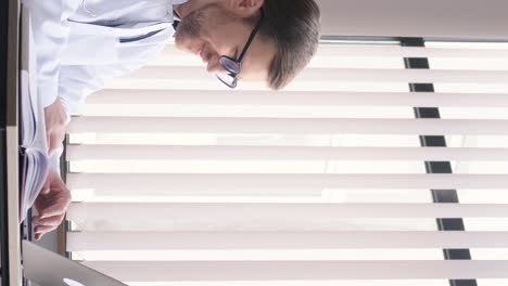 serious therapist writes a report or consults a patient online, fills out a medical card. focused young doctor in glasses working on laptop.