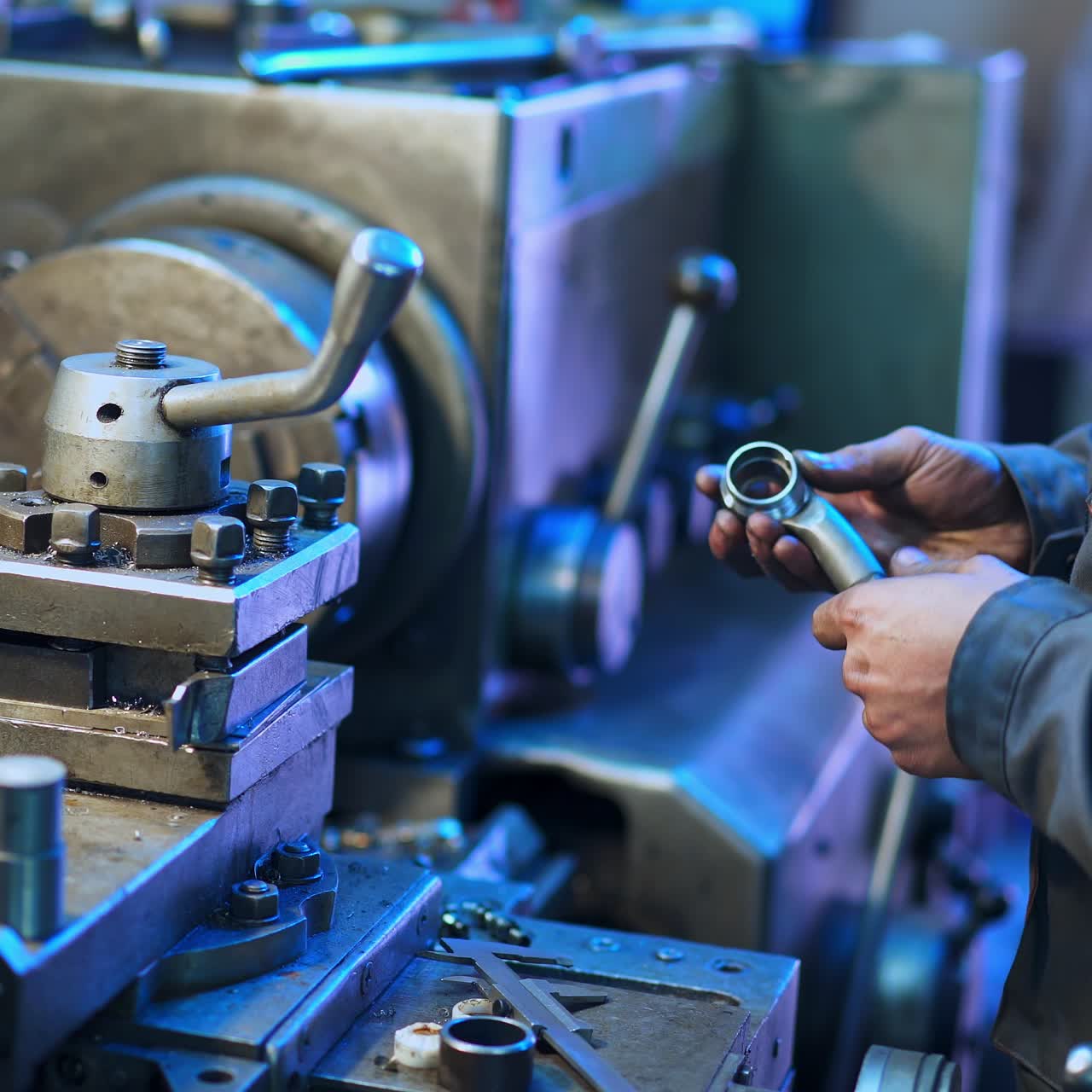 Turner in the uniform standing at his workplace. Man holding a metal detail and examining it. Turner's workshop background