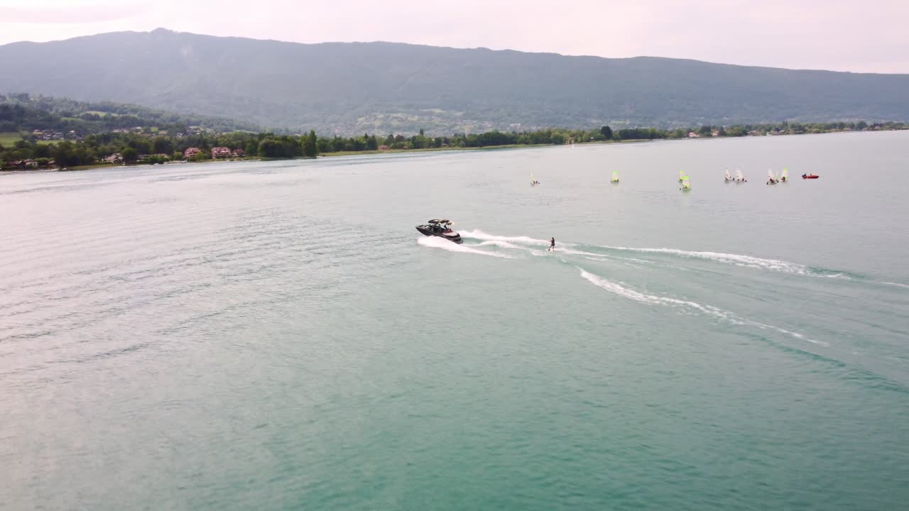 Aerial footage following a speed boat and wake boarder riding on Lake Annecy in Southern France. The drone starts behind the water sport the moves to the left while rotating right and moving away