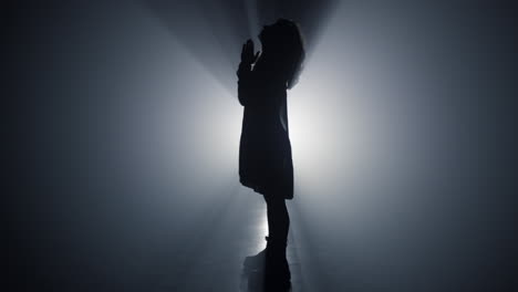 silhouette praying woman in darkness. religious girl folding hands for prayer.