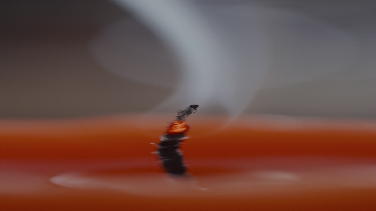 Stoppino di candela fumante con scia di fumo dopo che la fiamma si è spenta.
