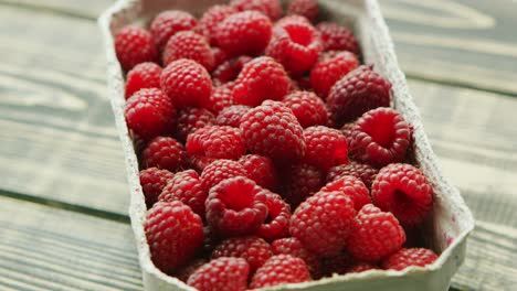 container with ripe raspberry on wooden desk