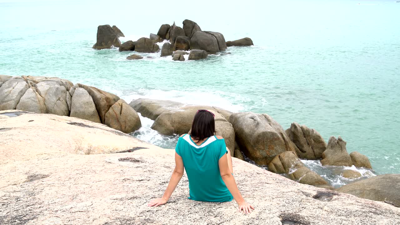 해변에 있는 돌 위에 앉아 있는 여자