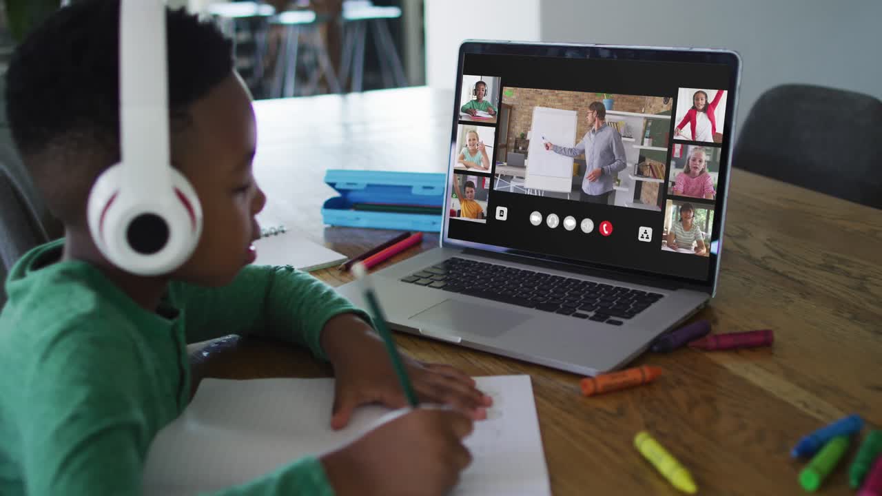 Schoolboy using laptop for online lesson at home, with diverse teacher and class on screen
