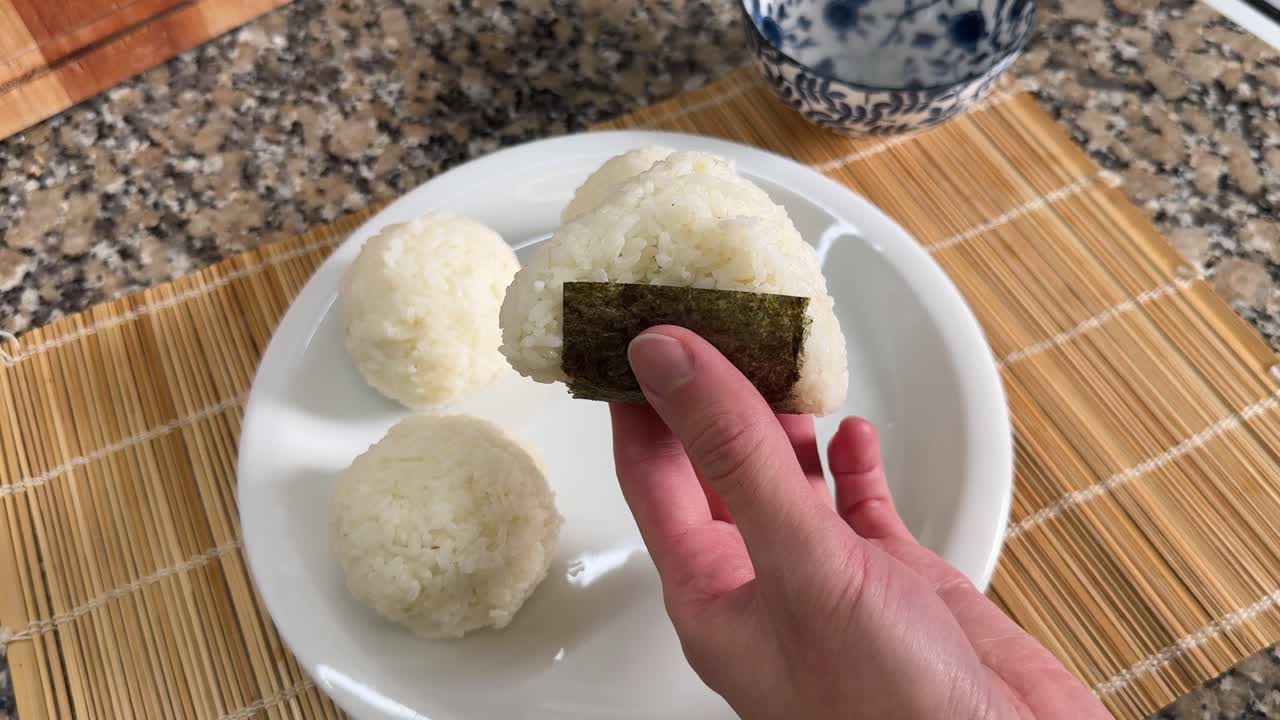 A Hand is Holding a Freshly Made Onigiri Wrapped With Seaweed - Close Up