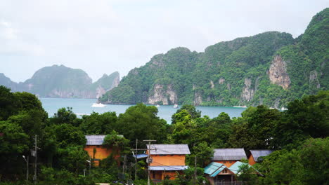 wide shot showing beautiful coastline and mountains of thailand, view from koh phi phi island - cruising boat and local houses on island