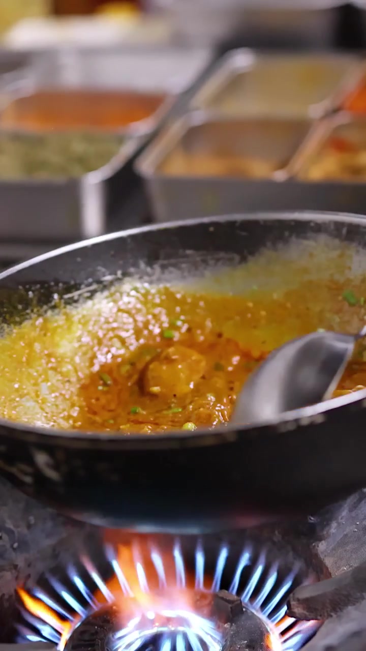 Primo piano di uno chef che mescola curry giallo in un wok su una fiamma blu di un fornello a gas.