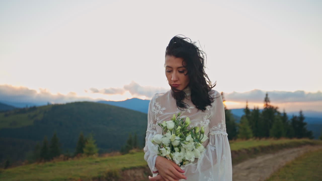 Bride in a White Dress with a Bouquet in Mountains at Sunset