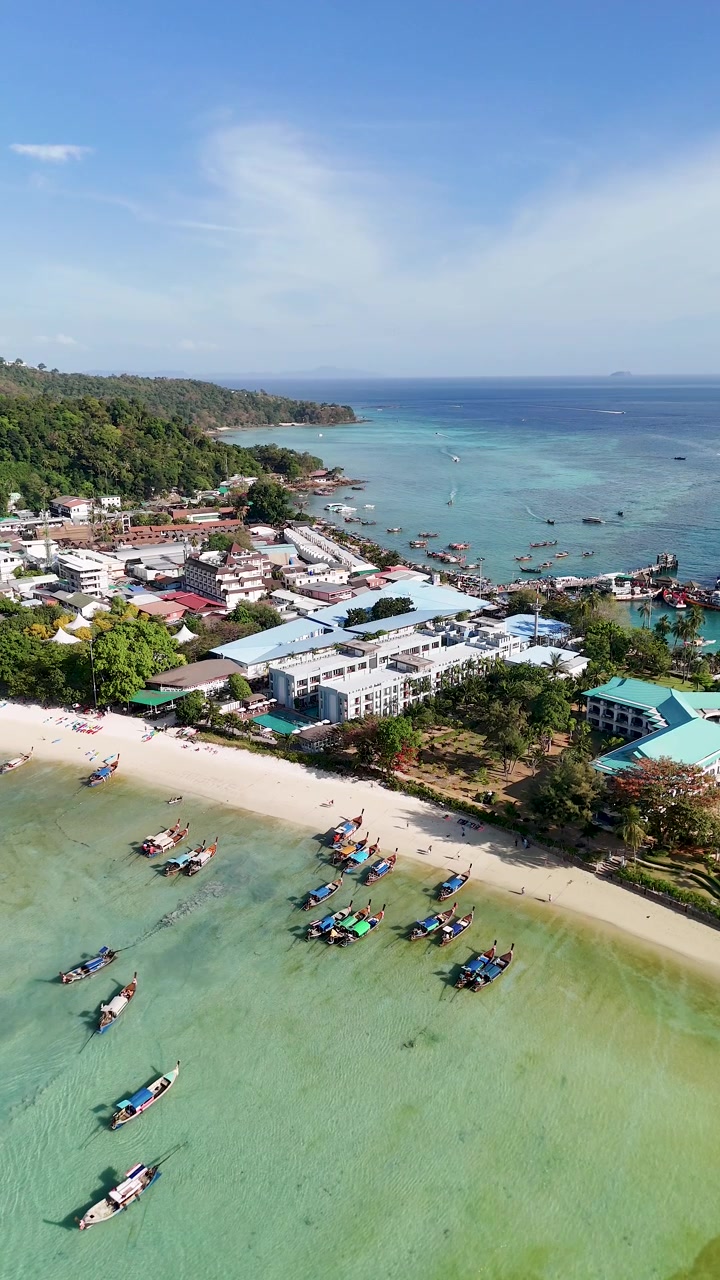 Ripresa aerea con drone di acqua turchese, spiaggia di sabbia bianca e tradizionali barche longtail thailandesi
