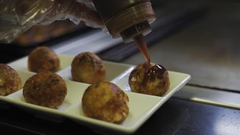 chef putting sauce in plated takoyaki balls