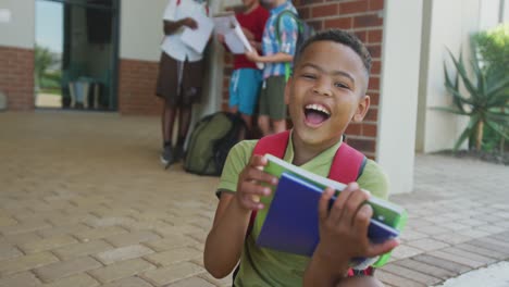 Video-of-happy-african-american-boy-holding-books-in-front-of-school