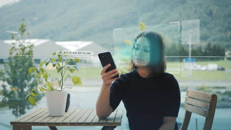 Young-woman-at-table-outside-use-smartphone-device-for-digital-biometric-facial-recognition,-pattern-access,-authentication-concept,-pixelated-face-security-system