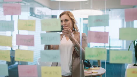 beautiful-business-woman-using-smartphone-taking-photo-of-sticky-notes-proud-of-successful-problem-solving-strategy-ideas-with-creative-mind-map-working-in-office-4k