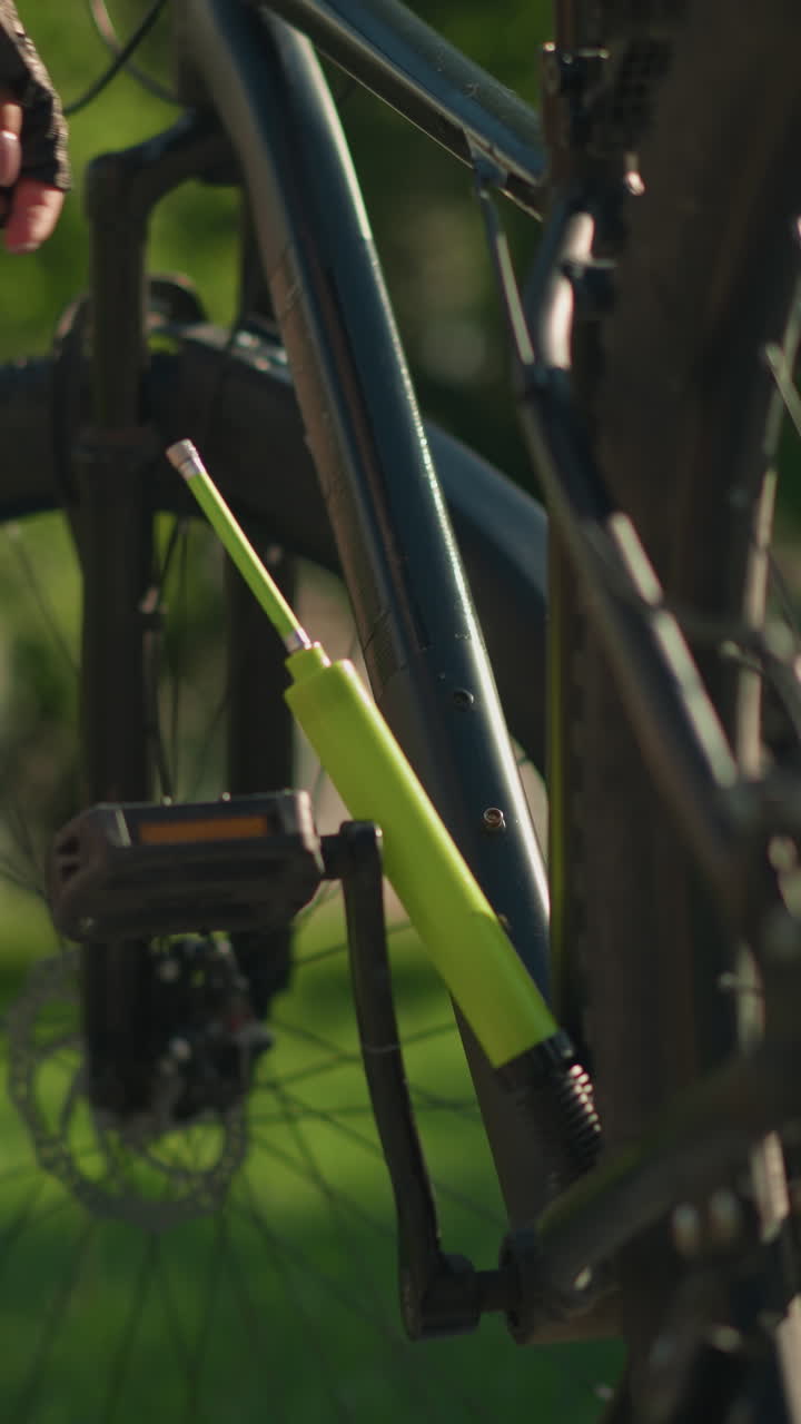 여성의 다리와 장갑을 입은 손은 은 날 페달 근처의 자전거에서 녹색 공기 프를 제거하고, 나무와 건물의 흐릿한 배경으로 활기찬 초록색을 배경으로 설정합니다.