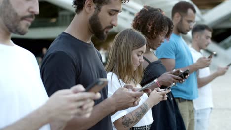 pensive young friends using smartphones on street