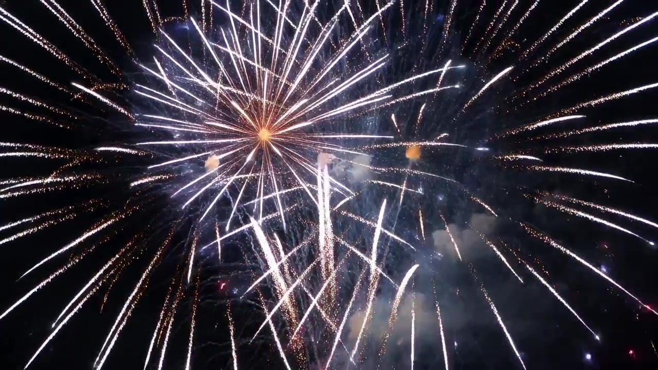 Fuochi d'artificio aerei che esplodono producendo esplosioni a strati e fontane nel cielo notturno, segnando il finale.
