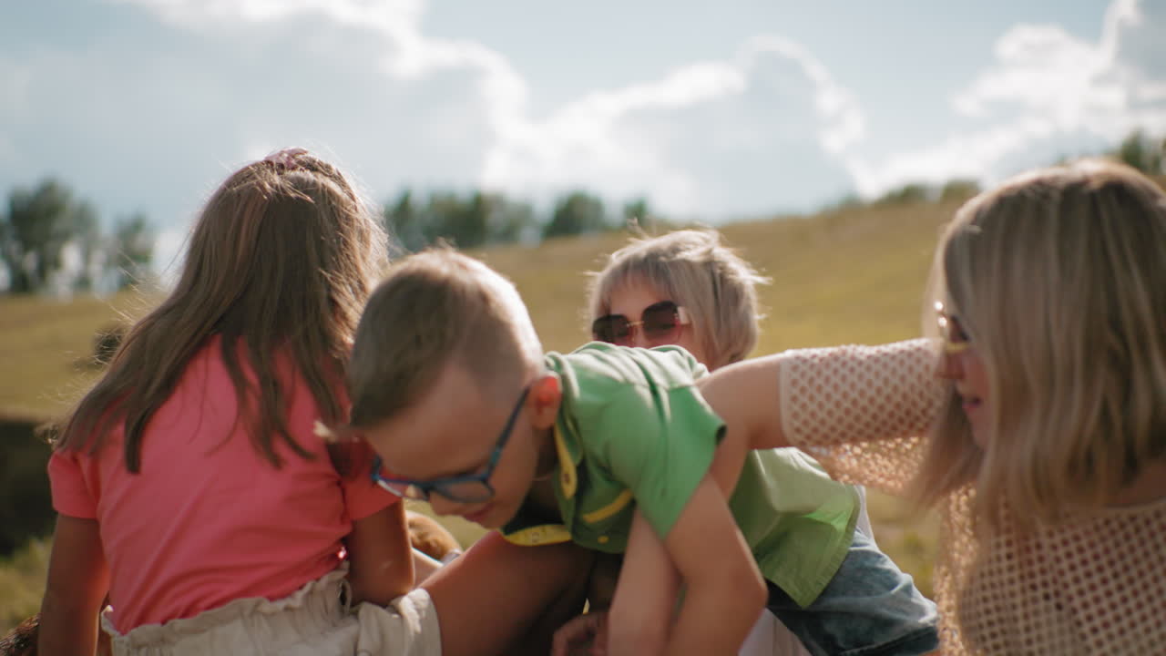 광활한 농장에서 이 비는 날에 가족이 즐거움을 즐기고, 을 오르는 아이들, 선글라스를 입은 여자가 웃고, 언덕과 나무가 배경, 황금 잔디, 따뜻한 시골.
