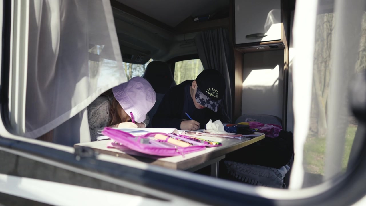 Due bambini fanno i compiti a un tavolo in un camper.
