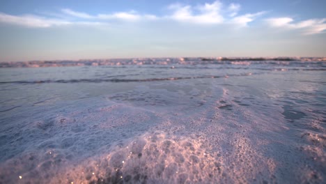 foamy ocean wave washing sandy beach under blue cloudy sky