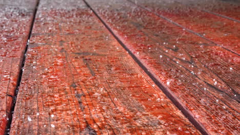 snow and hail falling on the planks of a red weatherproof wooden patio deck during a cold winter storm