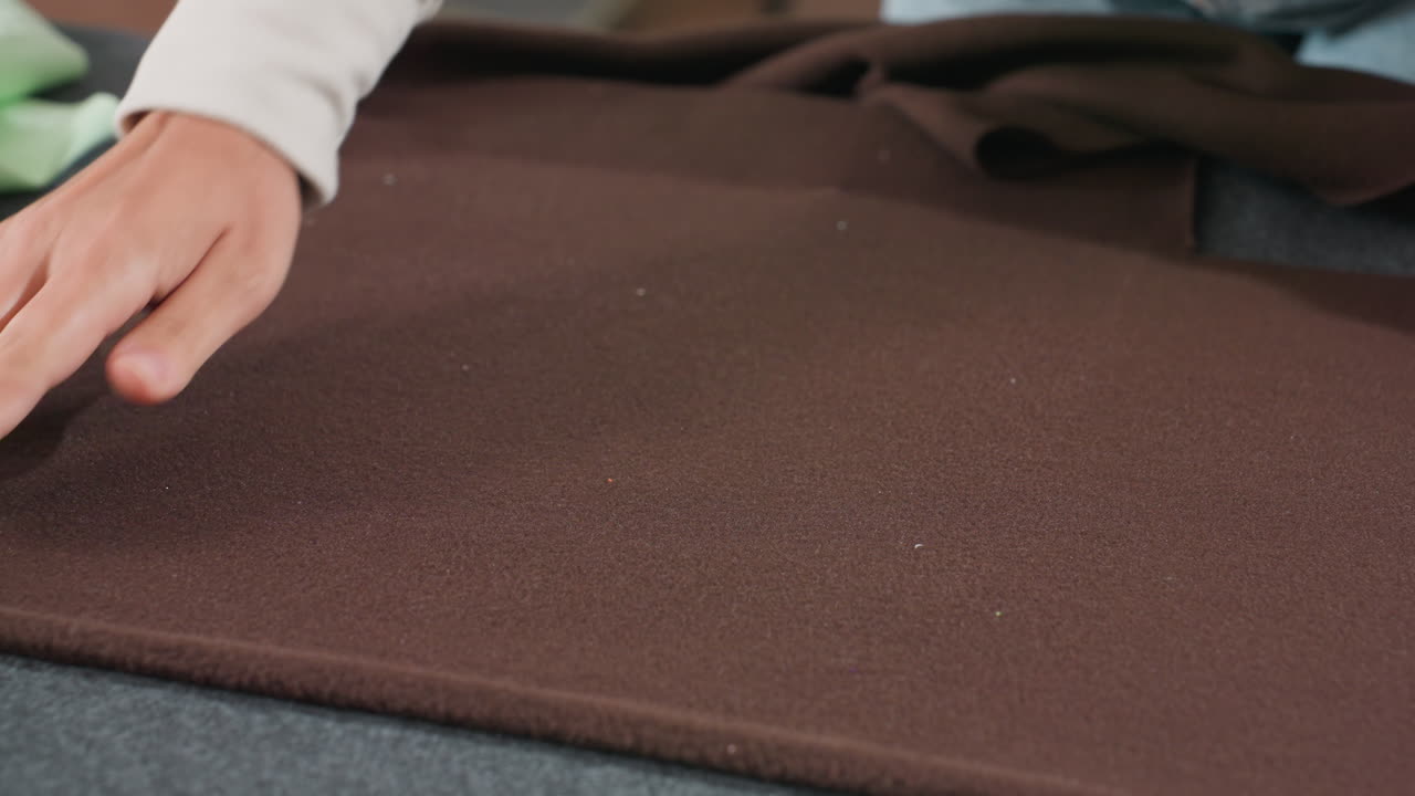 Close up view of costumer placing pattern design carefully on thick dark purple fabric during garment preparation process inside sewing workshop workspace focusing on accurate arrangement for cutting