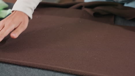 close up view of costumer placing pattern design carefully on thick dark purple fabric during garment preparation process inside sewing workshop workspace focusing on accurate arrangement for cutting