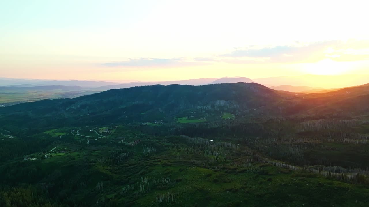 Aerial flyover of twilight hills in Steamboat Springs with lingering sunset light and forest, panoramic pullback across landscape