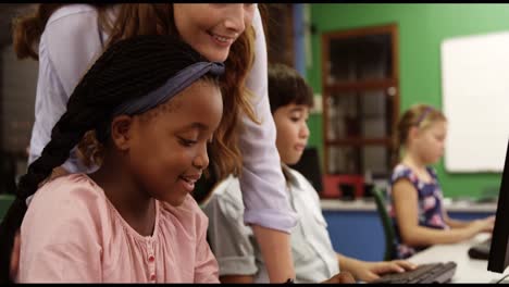 Teacher assisting school kids on personal computer in classroom