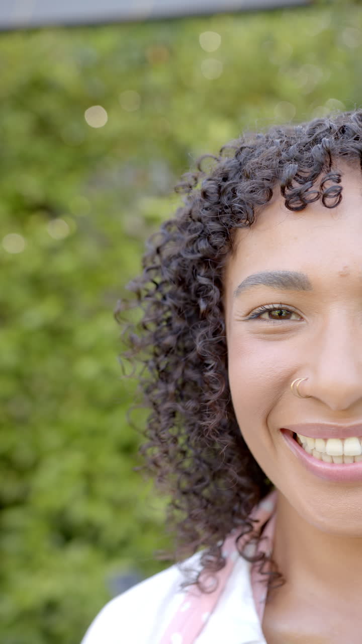Vertical video: Smiling woman with curly hair and nose ring enjoying time outdoors