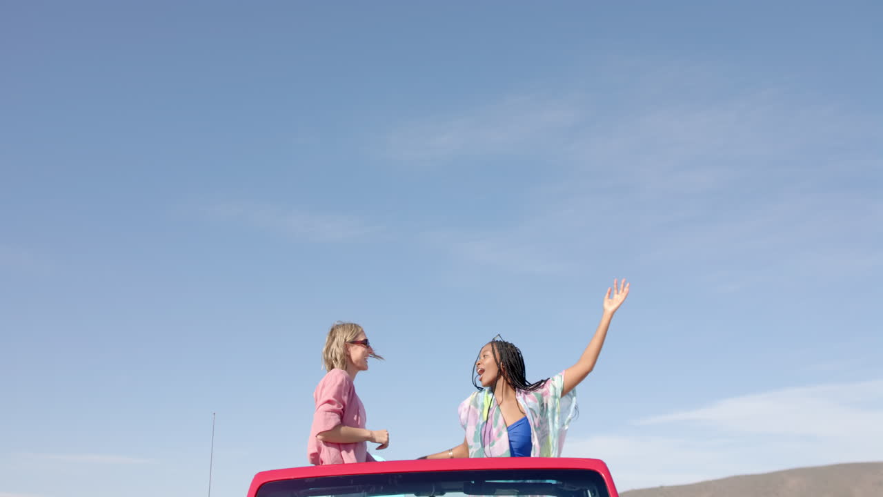 Giovani donne afroamericane e caucasiche si godono una giornata di sole durante un viaggio on the road con spazio per il testo