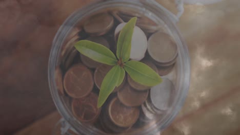 Digital-composition-of-thunderstorm-in-the-sky-against-plant-and-coins-in-glass-jar-on-wooden-surfac