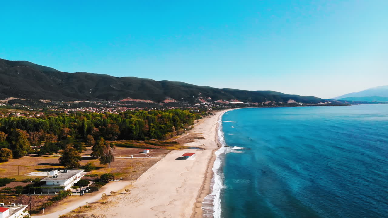 Aerial view of Aegean sea coast, long beach with waves and foam, greenery on the left