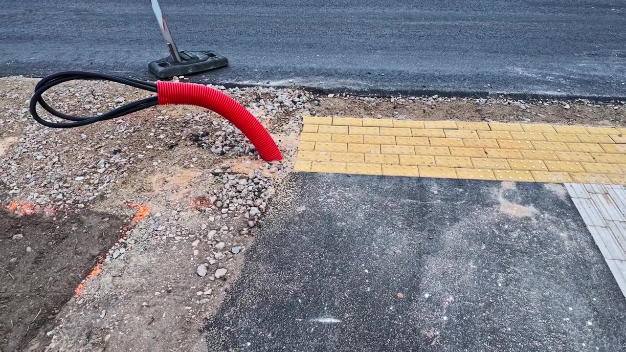Graving og legging av fiberoptiske kabler i et rødt korrugert trekkerør på en veibyggingsplass.