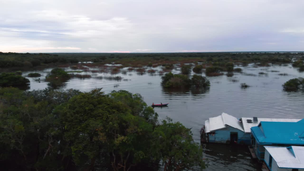 An aerial drone shot over a partially submerged forest in Cambodia, with small boats navigating through the trees, showcasing the region's unique seasonal flooding and natural beauty.